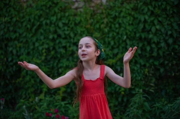 Kleines Mädchen auf der Straße vor grünem Laub. Mädchen mit langen Haaren. Kind im Alter von 9-10 Jahren — Stockfoto