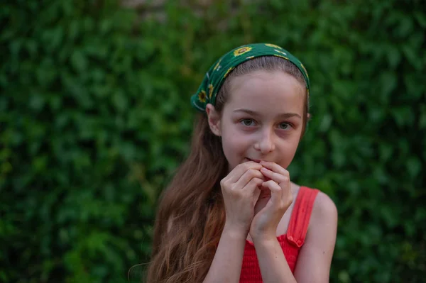 Egy kislány az utcán, zöld lombozat hátterében. Hosszú hajú lány. 9-10 éves gyermek — Stock Fotó