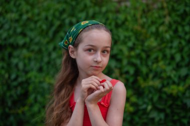 Sokaktaki küçük kız yeşil yapraklı bir arka plana karşı. Uzun saçlı kız. Çocuk 9-10 yaşlarında.