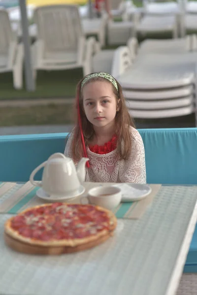 咖啡馆里拿着披萨的年轻女人的画像。9岁的女孩在暑期咖啡馆里吃披萨 — 图库照片
