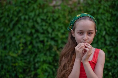 Sokaktaki küçük kız yeşil yapraklı bir arka plana karşı. Uzun saçlı kız. Çocuk 9-10 yaşlarında.
