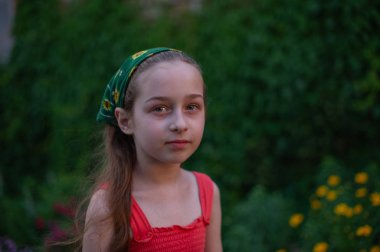 Sokaktaki küçük kız yeşil yapraklı bir arka plana karşı. Uzun saçlı kız. Çocuk 9-10 yaşlarında.