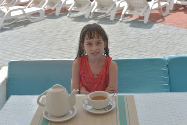 Une fillette de 9 ans boit du thé noir dans un parc aquatique ou en vacances au bord de la piscine. L'enfant se repose en été . — Photo