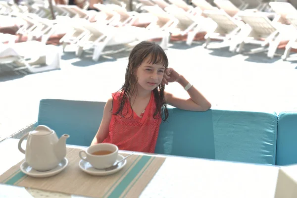 Una niña de 9 años bebe té negro en un parque acuático o de vacaciones en la piscina. El niño descansa en verano . —  Fotos de Stock