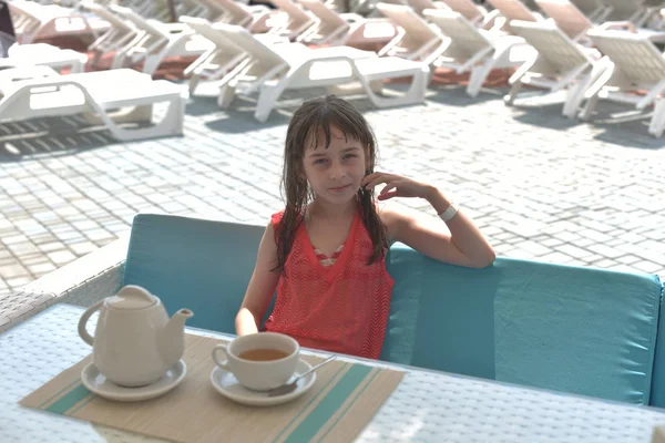 Une fillette de 9 ans boit du thé noir dans un parc aquatique ou en vacances au bord de la piscine. L'enfant se repose en été . — Photo