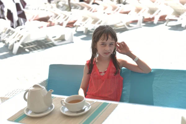 Una niña de 9 años bebe té negro en un parque acuático o de vacaciones en la piscina. El niño descansa en verano . —  Fotos de Stock