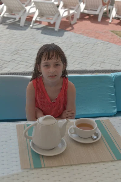 Uma menina de 9 anos bebe chá preto em um parque aquático ou de férias na piscina. A criança tem um resto no verão . — Fotografia de Stock