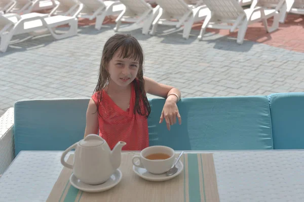 Une fillette de 9 ans boit du thé noir dans un parc aquatique ou en vacances au bord de la piscine. L'enfant se repose en été . — Photo