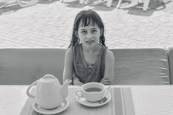 Una niña de 9 años bebe té negro en un parque acuático o de vacaciones junto a la piscina.Fotos en blanco y negro — Foto de Stock