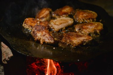 Pirzolalar ateşte kızardı. Tavada et pişiriyor.