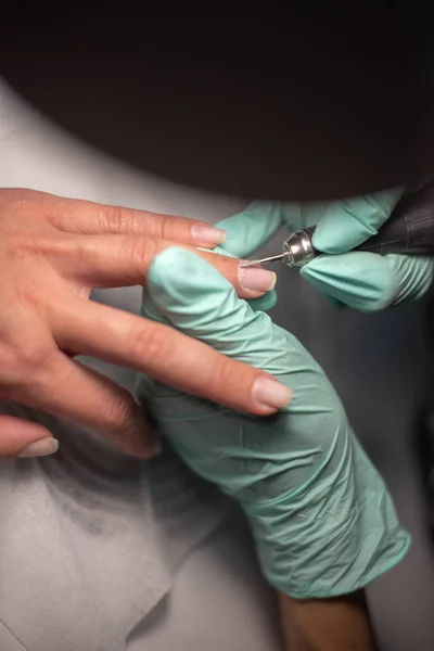 Une main de manucure avec un clou repose sur une main de manucure en gants hygiéniques bleus . — Photo