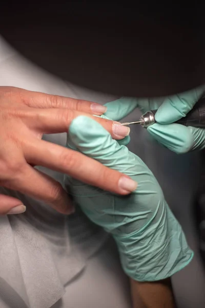 Eine Manikürhand mit Nagel liegt auf einer Manikürhand in blauen Hygienehandschuhen. — Stockfoto