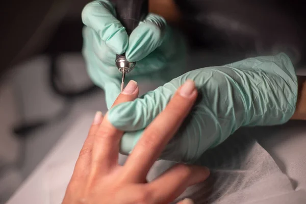 Eine Manikürhand mit Nagel liegt auf einer Manikürhand in blauen Hygienehandschuhen. — Stockfoto