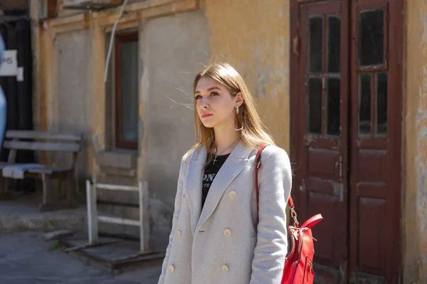 Élégante jeune jolie fille dans un manteau gris regarde la caméra et sourit légèrement sur le fond de la ville . — Photo