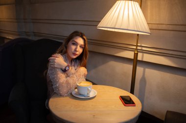 Kafedeki genç ve güzel kadın. Grunge. Kafede bej bluzlu bir kız. Kafede kahve içen bir kız. Latte, cappuccino