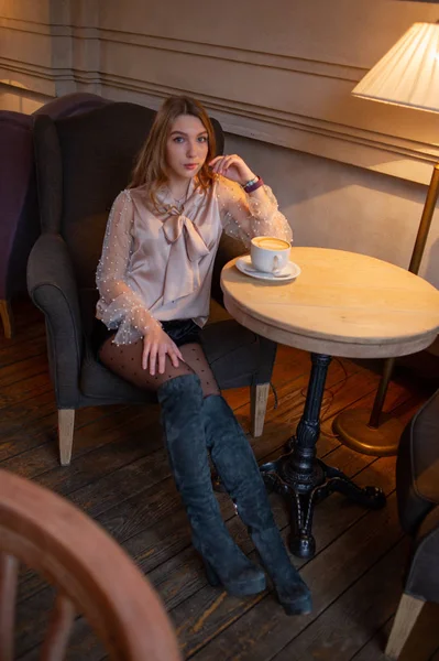 Una joven y bonita mujer en la cafetería. Grunge. Chica en un café con una blusa beige. Una chica bebe café en un café. Latte, Cappuccino — Foto de Stock