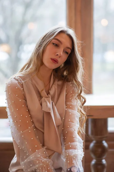 Una joven y bonita mujer en la cafetería. Grunge. Chica en un café en una blusa beige — Foto de Stock