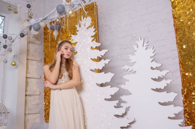 Parlak bir gece elbisesi giyen kız. Noel arifesi. Kürk ağacında rahat bir tatil Işıklar ve altın dekorla