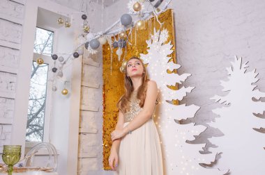 Parlak bir gece elbisesi giyen kız. Noel arifesi. Kürk ağacında rahat bir tatil Işıklar ve altın dekorla