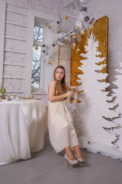 Dziewczyna w błyszczącej sukni wieczorowej. Wigilia. Przytulne wakacje na drzewie futerkowym ze światłami i złotym wystrojem — Zdjęcie stockowe