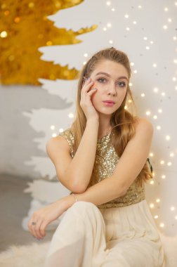 Parlak bir gece elbisesi giyen kız. Noel arifesi. Kürk ağacında rahat bir tatil Işıklar ve altın dekorla