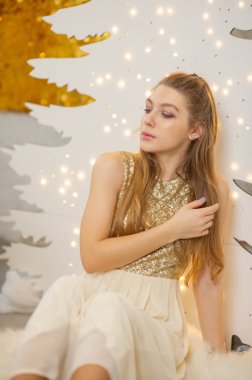 Parlak bir gece elbisesi giyen kız. Noel arifesi. Kürk ağacında rahat bir tatil Işıklar ve altın dekorla