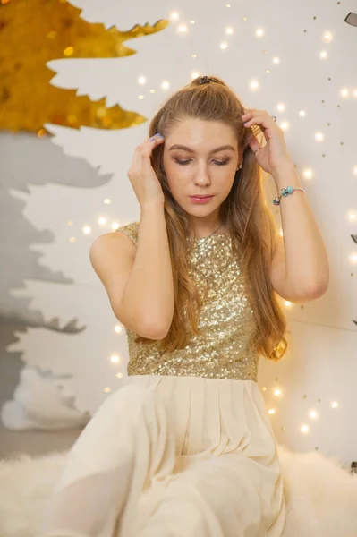 Menina em um vestido de noite brilhante. Véspera de Natal. Férias acolhedoras na árvore de peles com luzes e decoração dourada — Fotografia de Stock