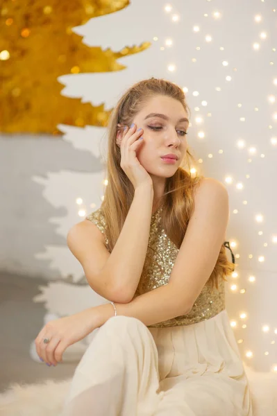 Mädchen in einem glänzenden Abendkleid. Heiligabend. Gemütlicher Urlaub an der Tanne mit Lichtern und Golddekor — Stockfoto