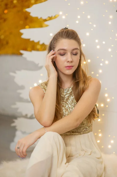 Chica en un vestido de noche brillante. Nochebuena. Acogedoras vacaciones en el árbol de piel con luces y decoración dorada — Foto de Stock