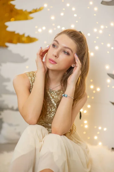 Chica en un vestido de noche brillante. Nochebuena. Acogedoras vacaciones en el árbol de piel con luces y decoración dorada — Foto de Stock