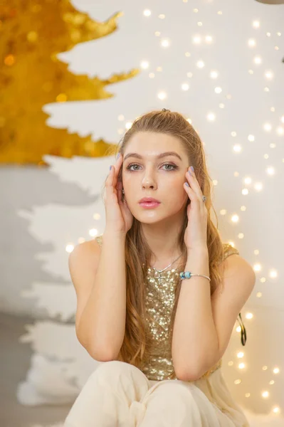 Chica en un vestido de noche brillante. Nochebuena. Acogedoras vacaciones en el árbol de piel con luces y decoración dorada — Foto de Stock