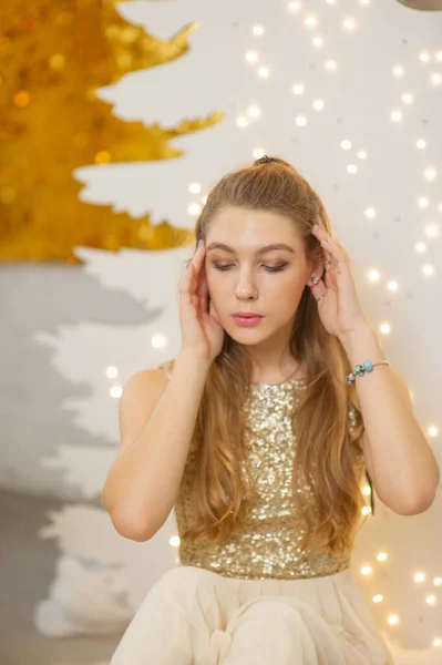 Chica en un vestido de noche brillante. Nochebuena. Acogedoras vacaciones en el árbol de piel con luces y decoración dorada — Foto de Stock