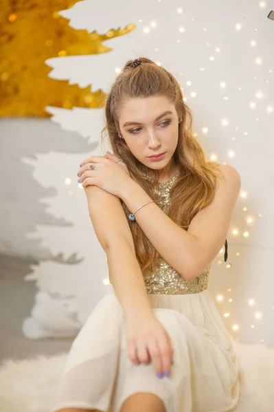 girl in a shiny evening dress. Christmas Eve. Cozy holiday at the fur-tree with lights and gold decor