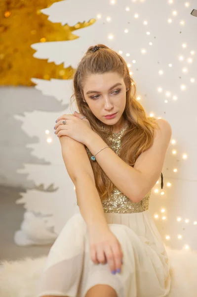Ένα κορίτσι με ένα λαμπερό βραδινό φόρεμα. Παραμονή Χριστουγέννων. Άνετο διακοπές στη γούνα-δέντρο με φώτα και διακόσμηση χρυσό — Φωτογραφία Αρχείου