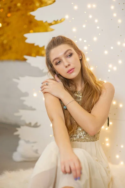 Ένα κορίτσι με ένα λαμπερό βραδινό φόρεμα. Παραμονή Χριστουγέννων. Άνετο διακοπές στη γούνα-δέντρο με φώτα και διακόσμηση χρυσό — Φωτογραφία Αρχείου