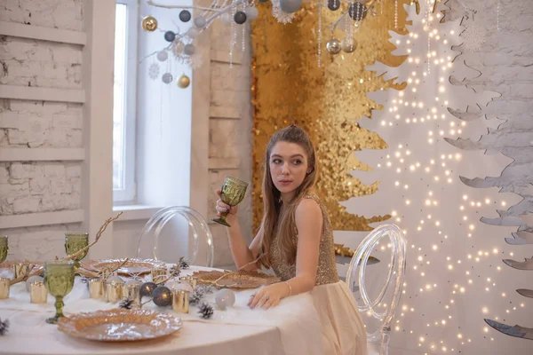 Mädchen in einem glänzenden Abendkleid. Heiligabend. Gemütlicher Urlaub an der Tanne mit Lichtern und Golddekor — Stockfoto