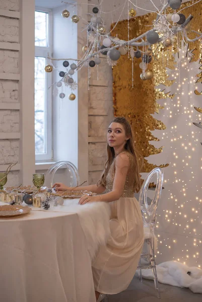 Mädchen in einem glänzenden Abendkleid. Heiligabend. Gemütlicher Urlaub an der Tanne mit Lichtern und Golddekor — Stockfoto