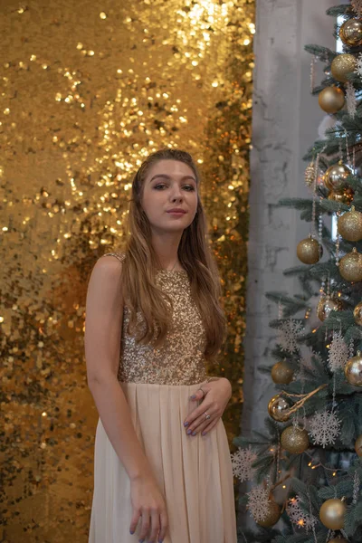 Menina em um vestido de noite brilhante. Véspera de Natal. Férias acolhedoras na árvore de peles com luzes e decoração dourada — Fotografia de Stock