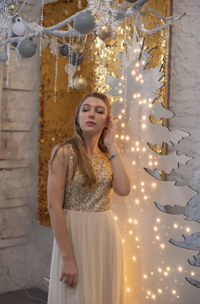 Menina em um vestido de noite brilhante. Véspera de Natal. Férias acolhedoras na árvore de peles com luzes e decoração dourada — Fotografia de Stock