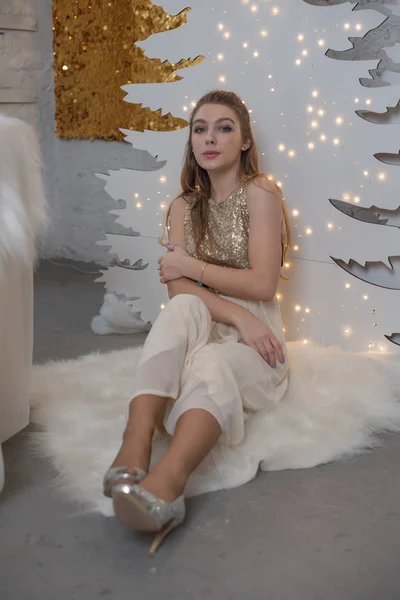 Chica en un vestido de noche brillante. Nochebuena. Acogedoras vacaciones en el árbol de piel con luces y decoración dorada —  Fotos de Stock