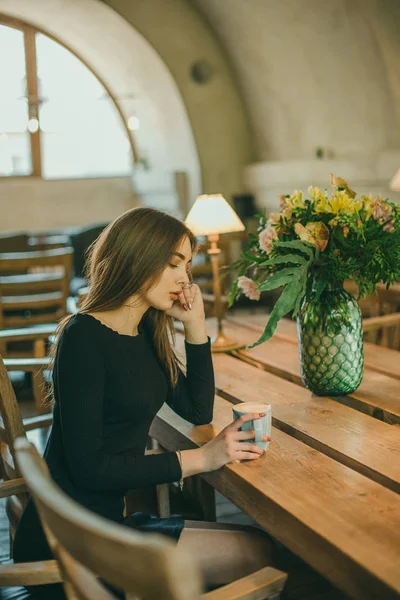 Schöne elegante brünette Mädchen in einem schwarzen Kleid entspannt in einem Straßencafé. Werbung, Mode. getöntes Foto — Stockfoto