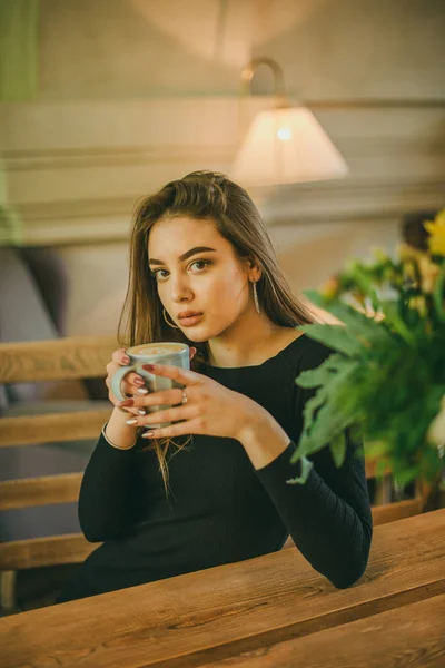 Schöne elegante brünette Mädchen in einem schwarzen Kleid entspannt in einem Straßencafé. Werbung, Mode. getöntes Foto — Stockfoto