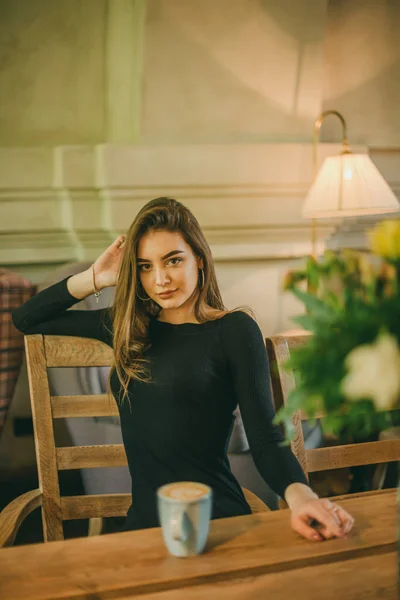 Mooi elegant brunette meisje draagt een zwarte jurk is ontspannen in een straat cafe. Reclame, mode. Getinte foto — Stockfoto