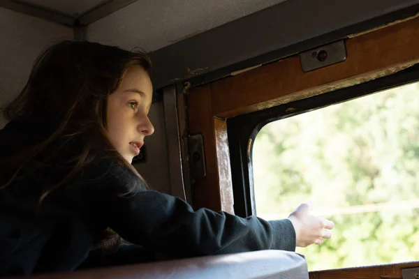 Linda chica acostada en el estante superior en el tren y mirando por la ventana a la calle. Vacaciones de verano — Foto de Stock