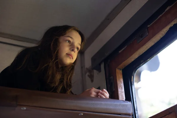 Linda chica acostada en el estante superior en el tren y mirando por la ventana a la calle. Vacaciones de verano — Foto de Stock