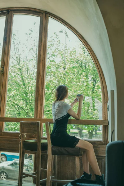 Schöne elegante brünette Mädchen in einem schwarzen Kleid entspannt in einem Straßencafé. Werbung, Mode. getöntes Foto — Stockfoto