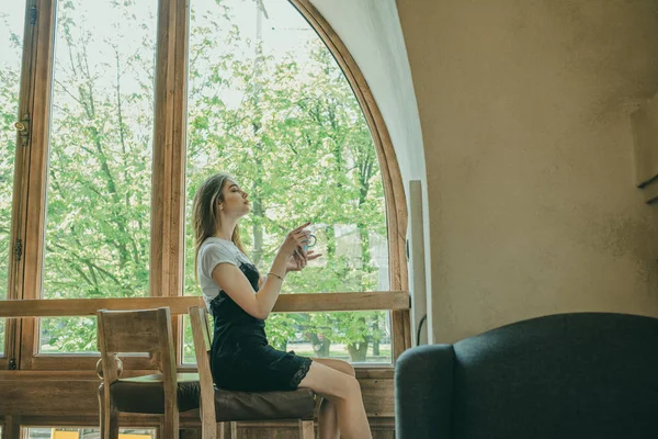 Schöne elegante brünette Mädchen in einem schwarzen Kleid entspannt in einem Straßencafé. Werbung, Mode. getöntes Foto — Stockfoto