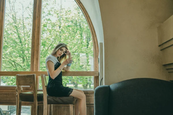 Schöne elegante brünette Mädchen in einem schwarzen Kleid entspannt in einem Straßencafé. Werbung, Mode. getöntes Foto — Stockfoto