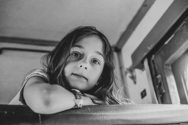 Chica acostada en el estante superior en el tren y mirando por la ventana a la calle. Verano. Foto en blanco y negro — Foto de Stock