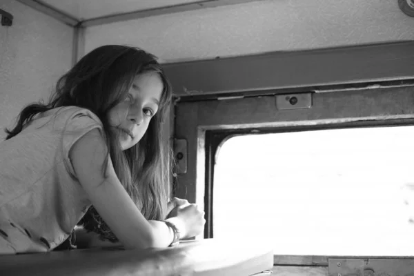 Nettes Mädchen, das auf dem obersten Regal im Zug liegt und aus dem Fenster auf die Straße blickt. Sommerferien. getöntes Foto — Stockfoto